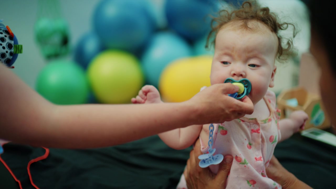 Baby with down syndrome getting physical therapy, a helping hand supporting the infant during developmental exercises