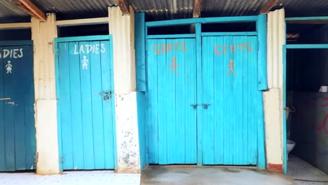 vista del baño turístico con puertas azules brillantes marcadas damas y caballeros en un área de kenia, áfrica