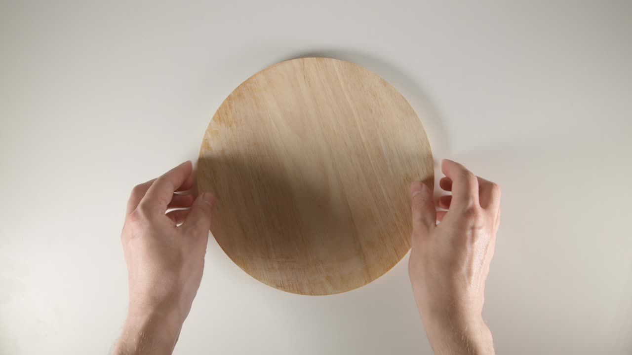 위쪽: 사람의 손이  테이블 위에 둥근 절단판을 놓습니다.