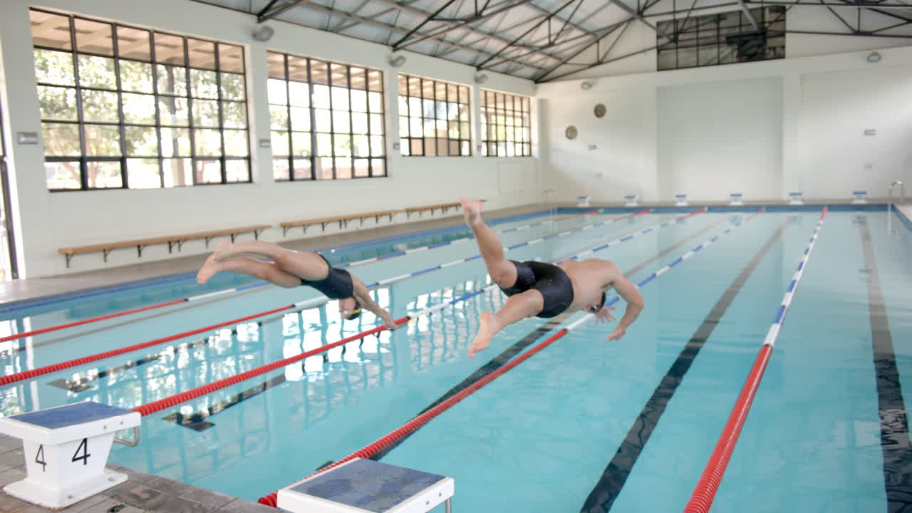 Diving into swimming pool, athletes practicing techniques in indoor facility