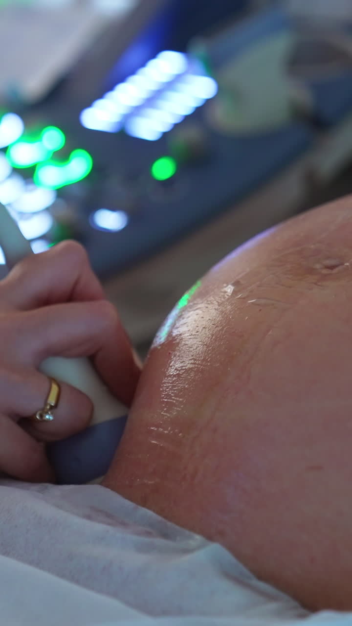 Ultrasonic diagnostics for a pregnant lady. Big round abdomen being checked by the device in doctor's hand. Close up. Vertical video