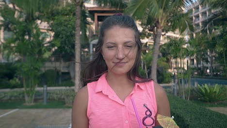 nice girl in pink blouse stands against palms smiling