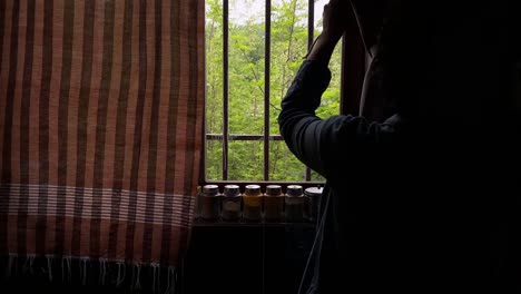 Young-curly-hair-woman-waking-up-after-sleeping-stands-up-from-bed-and-opening-kitchen-curtains-looking-at-window-spice-shelf-home-in-sunny-morning