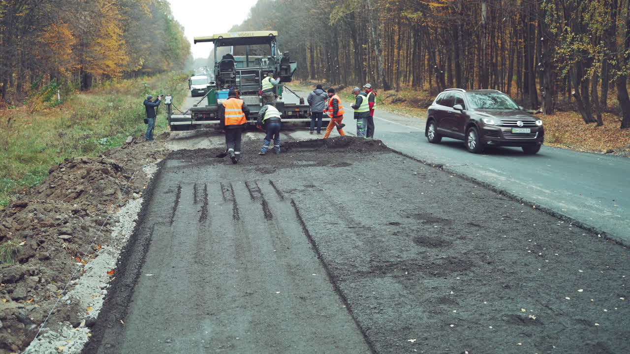 Asphalt pavers working on construction site. Brigade of workers repairs road under the program of planned repair