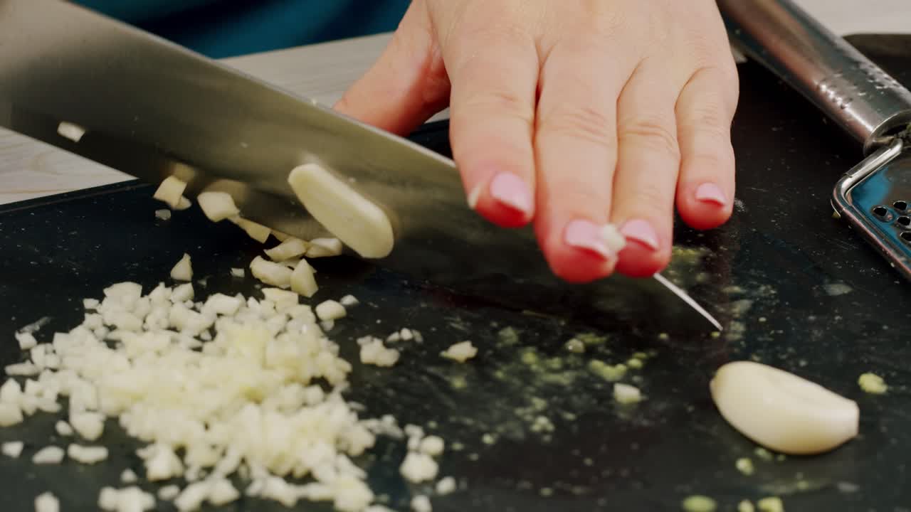 Woman chopping garlic on wooden cutting board at domestic kitchen. High quality 4k footage