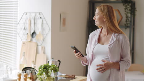 hermosa mujer embarazada usando un teléfono inteligente en la cocina