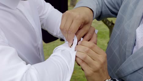 the best man, dressed in a suit, adjusts the groom's cufflinks during wedding preparations