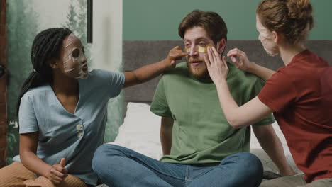 three rommates applying facial mask sitting on the bed in bedroom