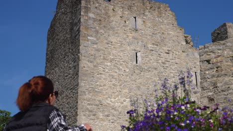 A female tourist takes a smartphone photo of a historic stone castle in Killarney, Ireland, on a beautiful sunny day. Perfect for travel and tourism content