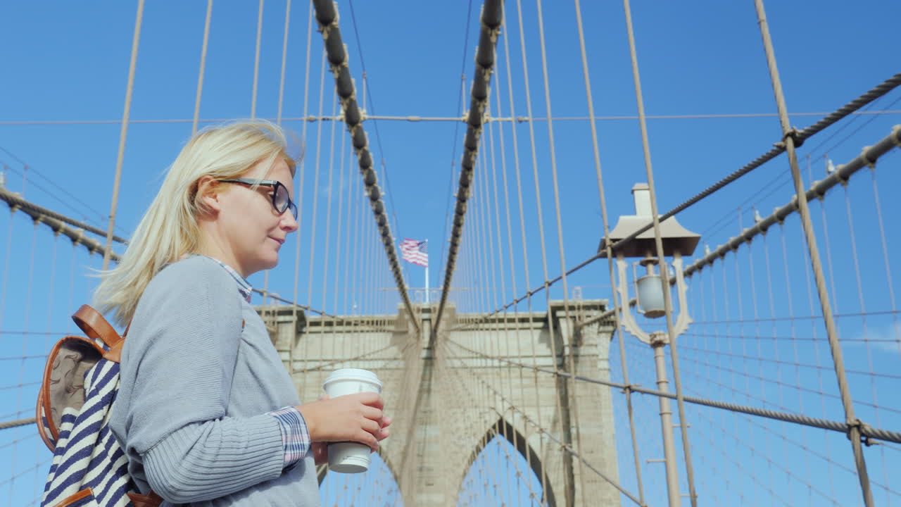 커피 한 잔을 손에 든 여자가 맨해튼이 내려다보이는 브루클린 다리에 서 있다