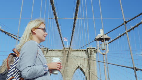 Eine-Frau-Mit-Einer-Tasse-Kaffee-In-Der-Hand-Steht-Auf-Der-Brooklyn-Bridge-Mit-Blick-Auf-Manhattan-S