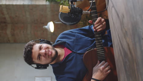 young man giving online guitar class in recording studio