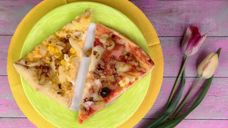 dos pedazos de pizza con tomates, salchichas, mozzarella y aceitunas en el plato gira lentamente sobre un fondo rosado.