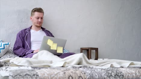 man working from bed in pajamas