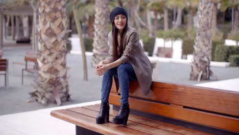 Fashionable-young-woman-sitting-waiting-on-a-bench