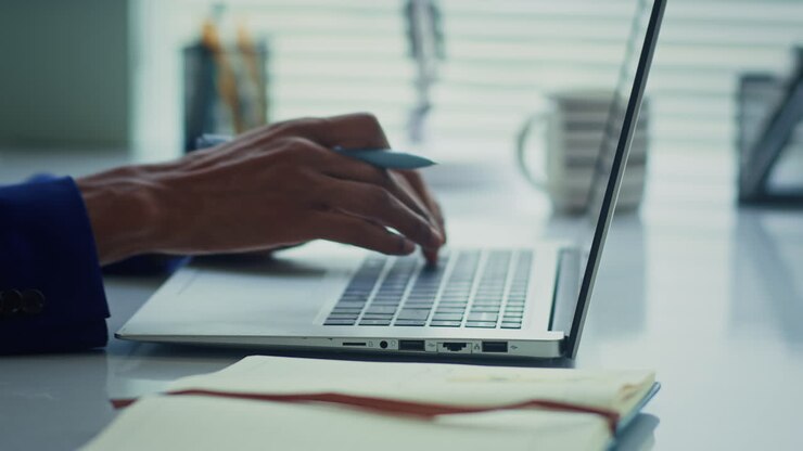 Hände eines nicht erkennbaren Managers, der eine E-Mail auf einem Laptop versendet