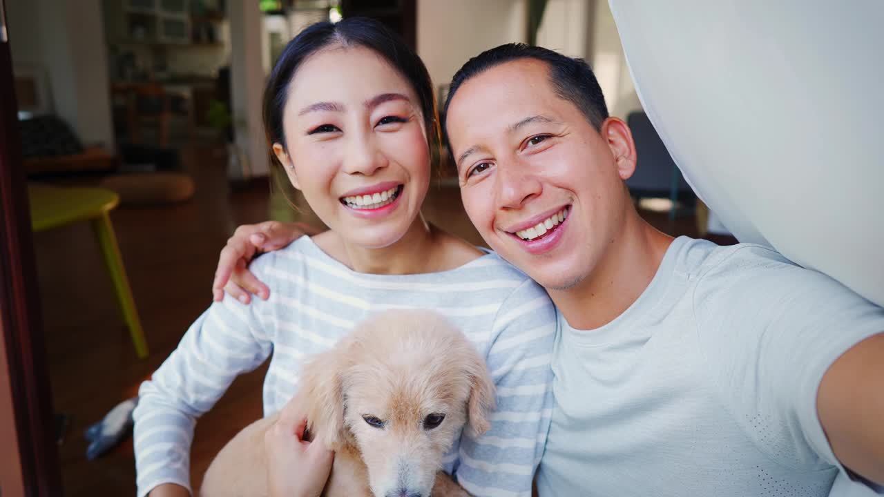 어린 아시안 커플이 강아지를 들고 드폰에서 셀피를 찍고, 가정의 인테리어가 배경입니다. 30대 성숙한 남녀와 개 애완동물이 가족 사진을 찍고 있습니다. - 행복한 그룹 초상화