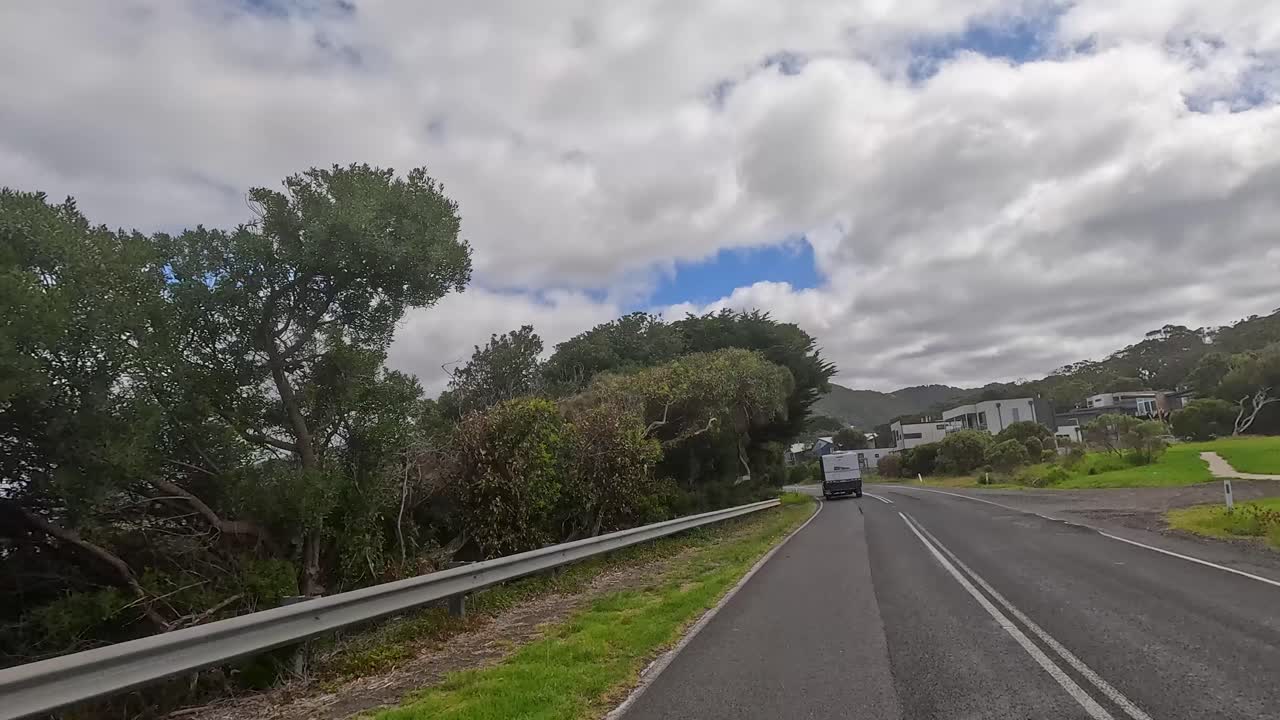 A 14-second drive along Great Ocean Road, showcasing lush greenery, coastal views, and passing vehicles under a partly cloudy sky