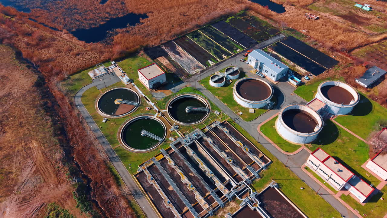 Wide aerial view of water reclamation facility and drying basins. Industrial site with circular clarifiers and dark sludge drying beds in daylight