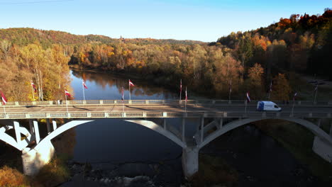 a truck crosses a bridge over a river surrounded by autumn foliage