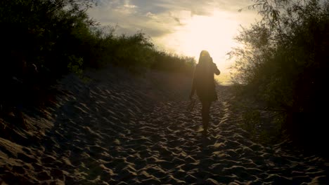 silhouette of a woman walking barefooted on country road against bright sunlight, full body shot