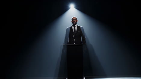 man speaking at a podium under spotlight