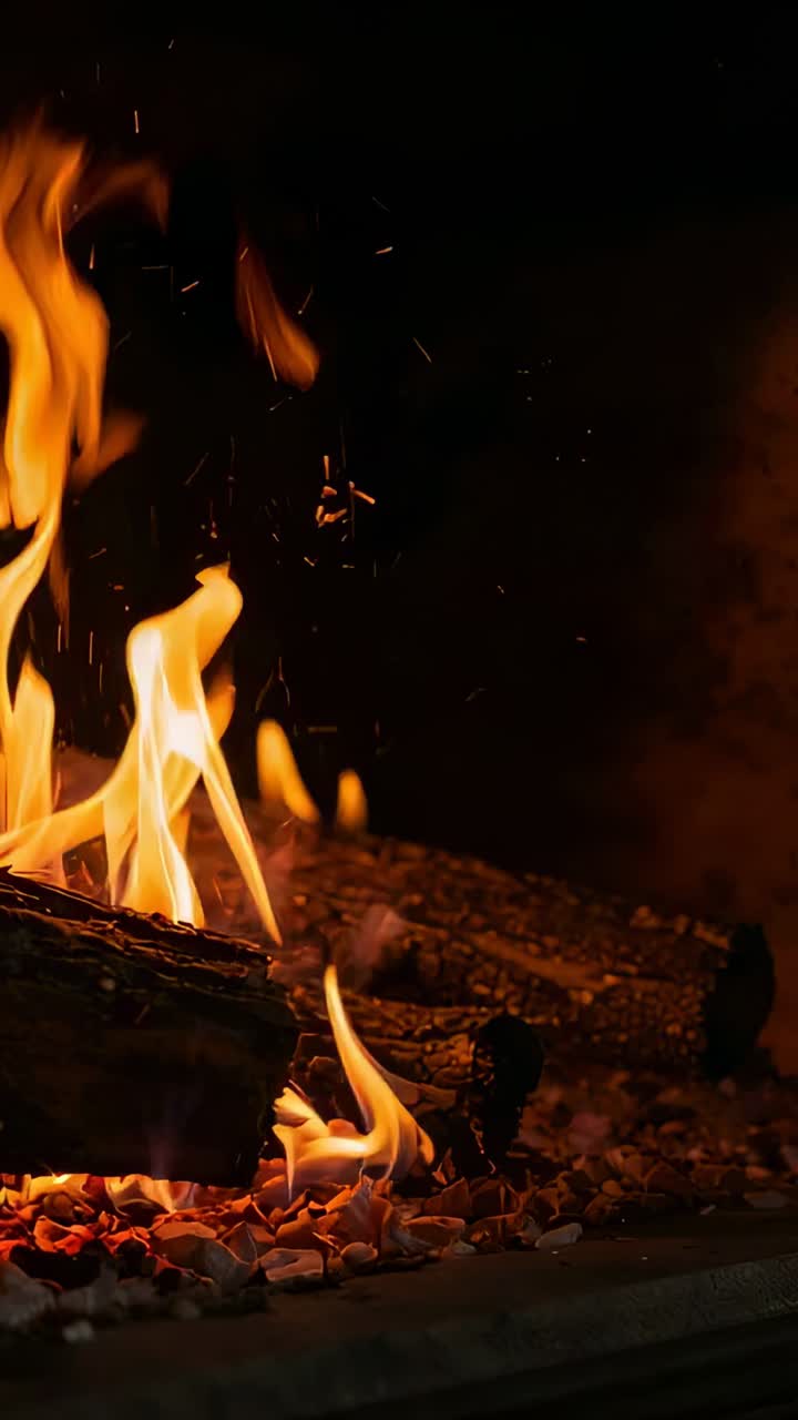 Vertical video: Embers igniting log, flames rising and shifting in home fireplace, creating glow