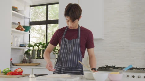 Asian-male-teenager-preparing-food-and-wearing-apron-in-kitchen