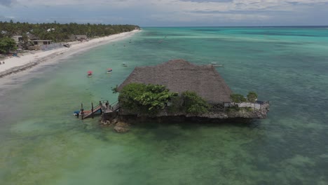 Aerial-orbiting-shot-of-The-rock-restaurant-in-ocean-during-sunny-day-in-Zanzibar,-Africa