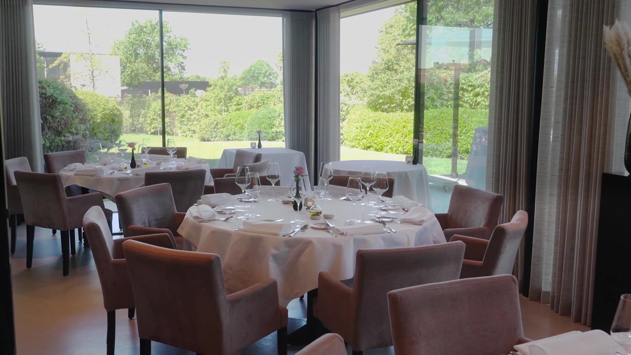 Naturskön vy över dekorerade middagsbord för evenemang inne i en lyxig restaurang med fönsterutsikt över en vacker trädgård.