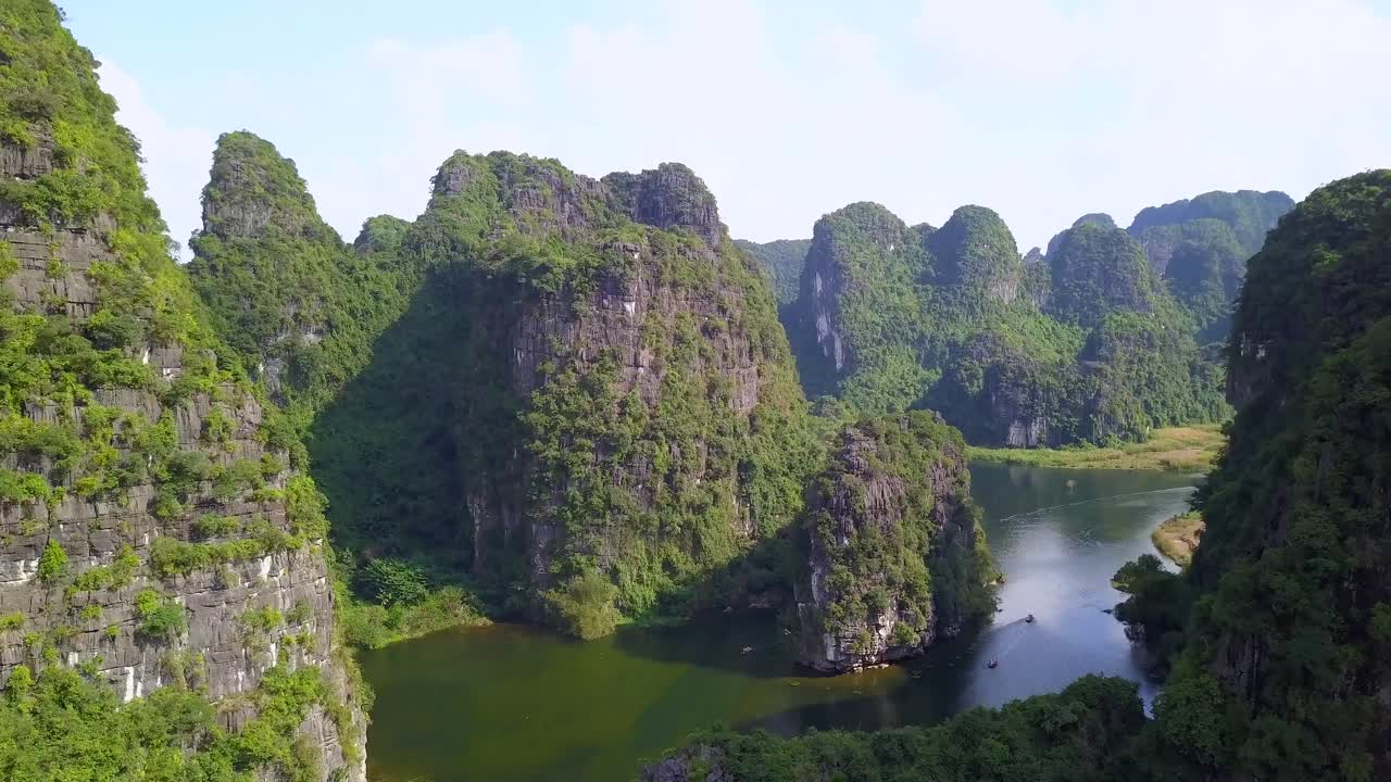 Cinematic drone footage of majestic green limestone peaks. Ricefields in the wild jungle in the spring with boat tour canal in Trang An, Ninh Binh, Vietnam