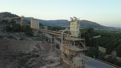 industrial quarry with conveyor belts and stone crusher amidst hills, showcasing heavy machinery and mining operations. drone shot moving away
