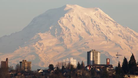 Epic-wide-shot-of-Tacoma-Skyline-Buildings-and-gigantic-snow-covered-Mount-Rainier-during-sunset-in-background