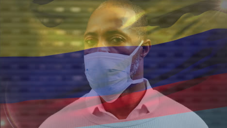 animation of waving colombia flag over portrait of african american man wearing face mask on street