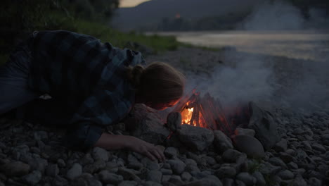 Man-lies-on-ground-blowing-deep-into-tipi-campfire-to-grow-the-flame-encompassing-the-sticks