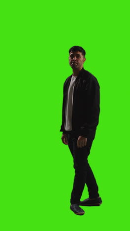 vertical video full length shot of man walking into frame standing and waiting against green screen with low key lighting