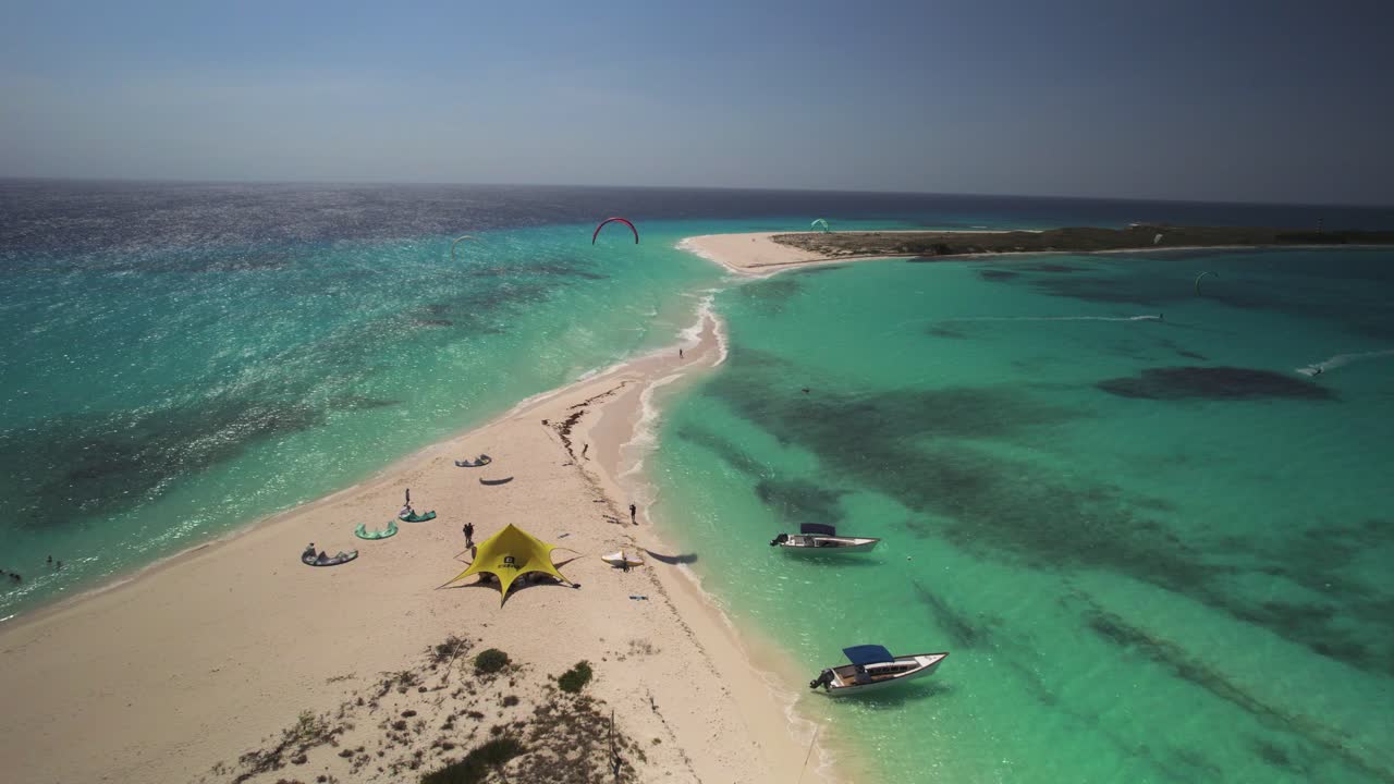 Una spiaggia tropicale con kitesurfer e barche in acque turchesi in una giornata di sole, vista aerea.