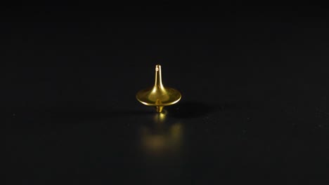 gold tops spinning and wobbling on black surface