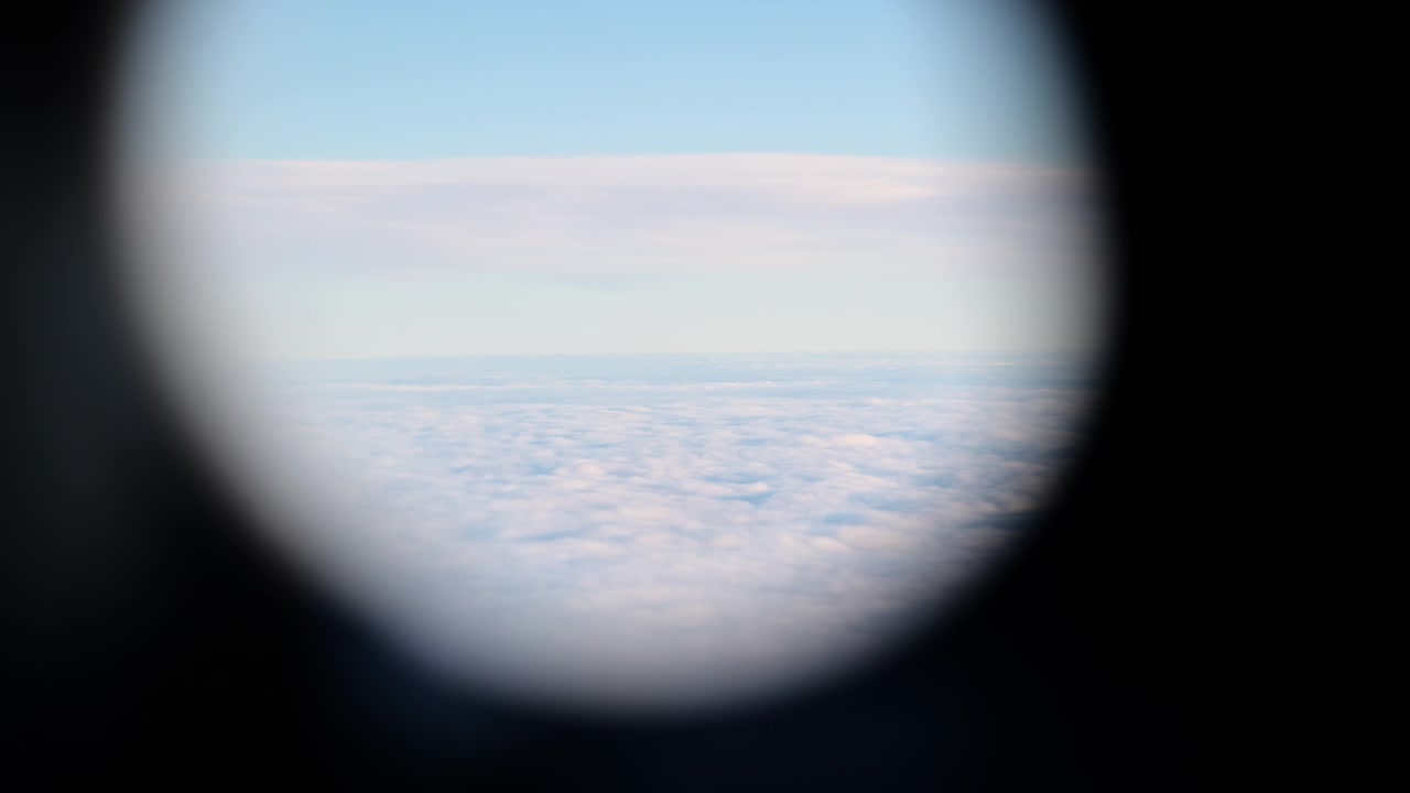 Udsigt gennem et flyvindue til et tykt lag hvide skyer nedenfor og blå himmel ovenfor