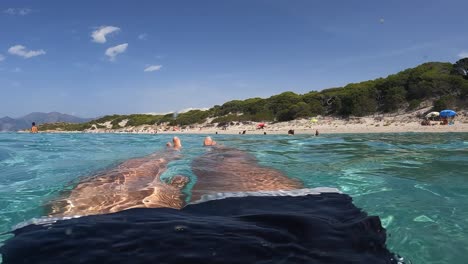 fpv of man legs and feet floating on beautiful clear and transparent seawater of turquoise lagoon of saleccia beach in corsica island, france