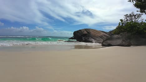 Cámara-Lenta-De-Olas-Rompiendo-En-La-Playa-De-Arena-Blanca-Y-Piedras-De-Granito-En-Un-Día-Soleado,-Mahe-Seychelles