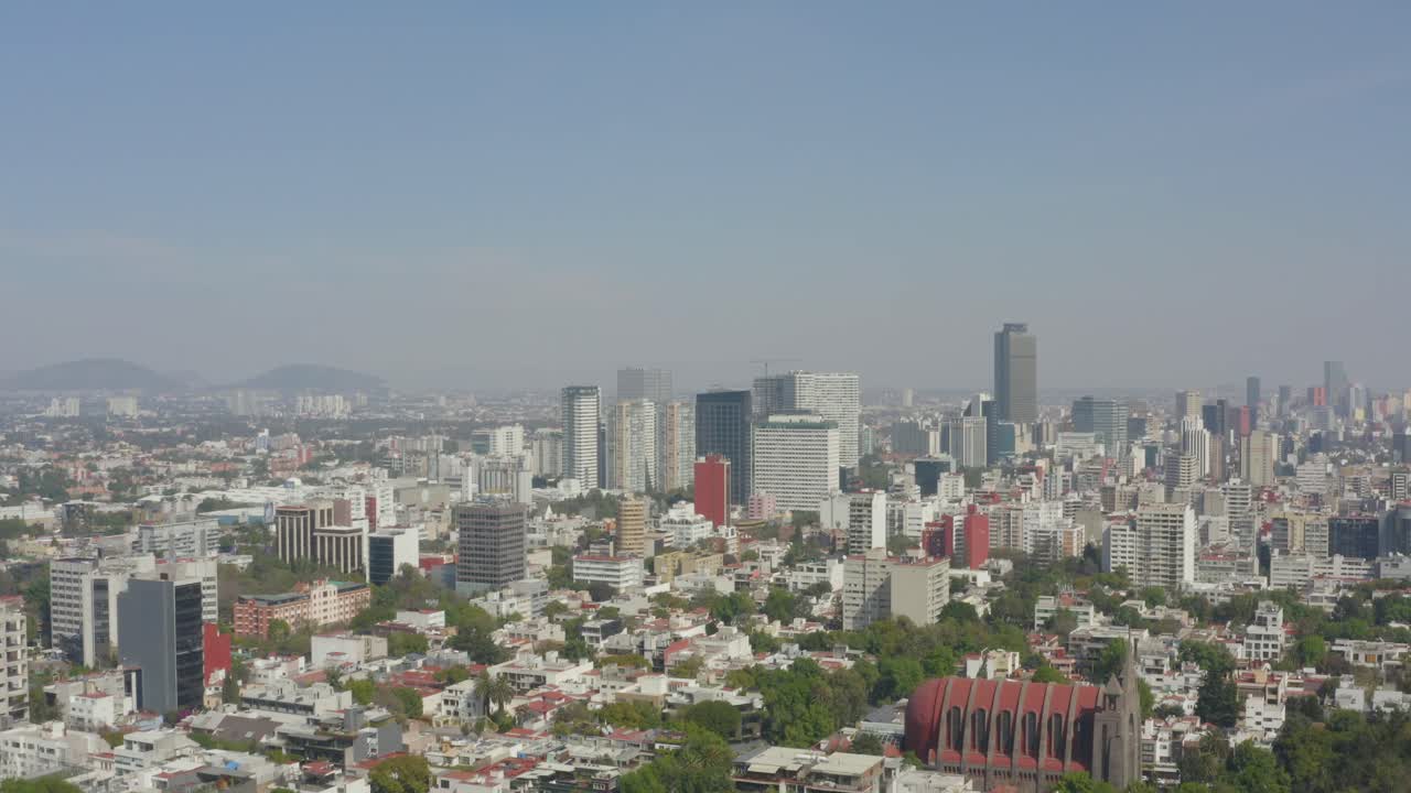Rising aerial shot of Mexico City skyline on a clear day with blue skies.
