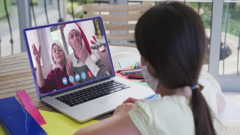 Caucasian-girl-wearing-face-mask,-on-laptop-video-chat-during-christmas-at-home