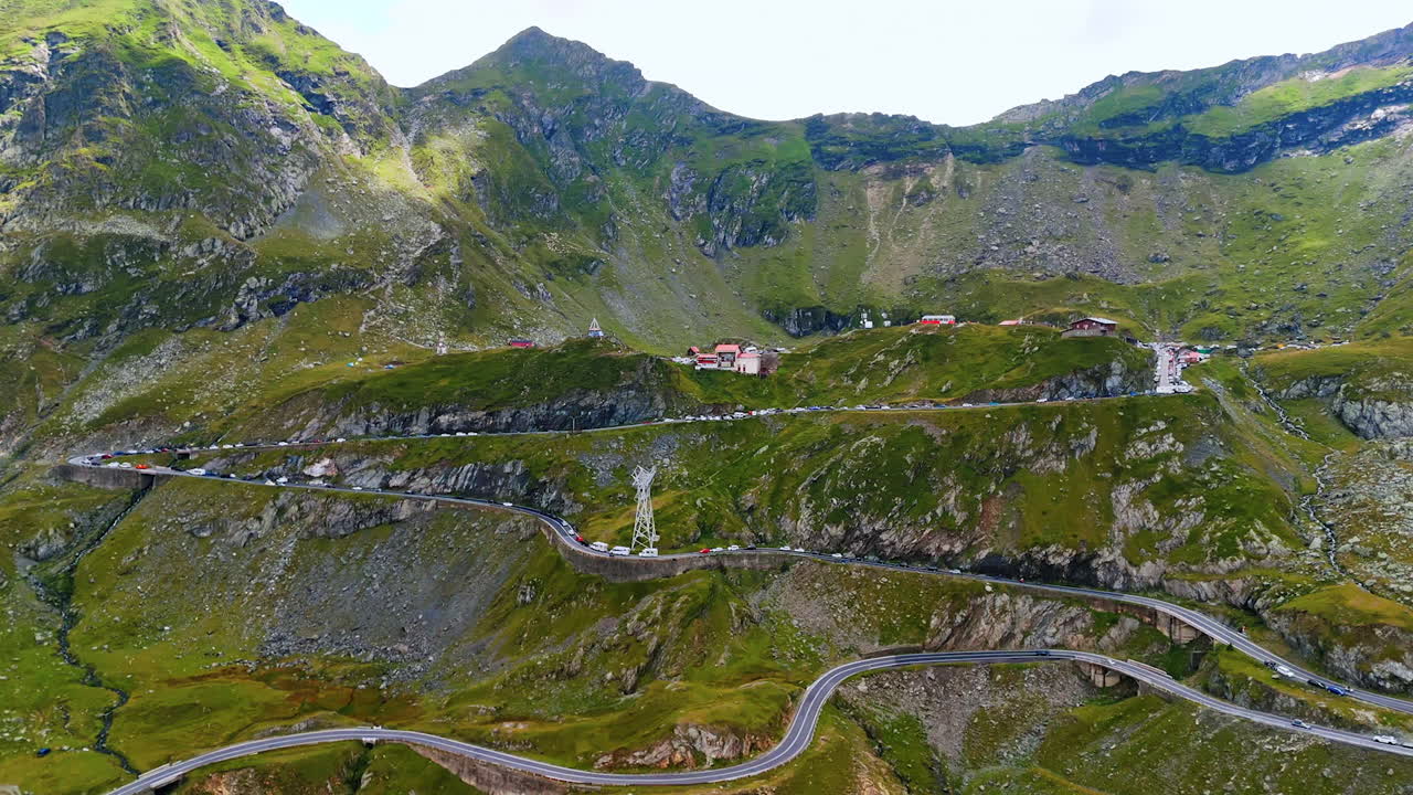 Approaching the picturesque slopes of the mountains with a highway. Multiple cars stand on the highway. Famous Transfagarash highway in Romania