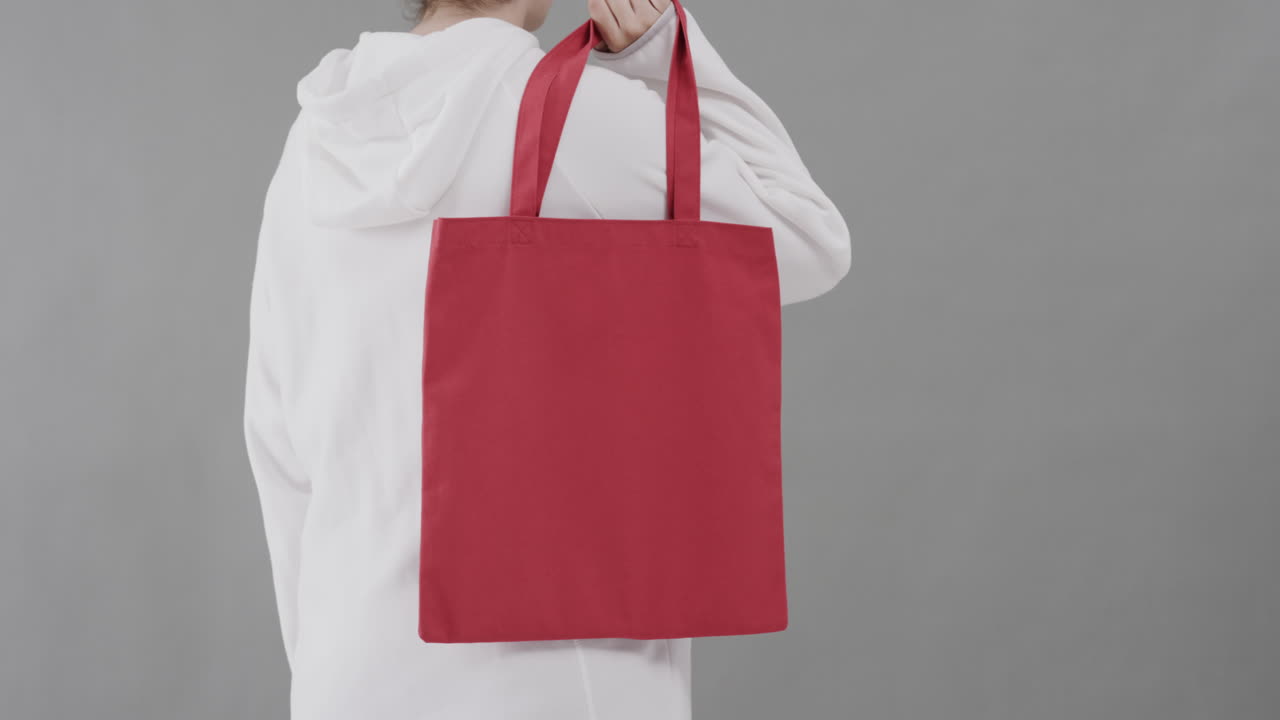 Mujer caucásica con sudadera blanca con capucha sosteniendo una bolsa roja sobre fondo gris, con espacio para texto, en cámara lenta