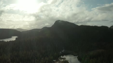 Calm-Lake-Surrounded-By-Coniferous-Trees-In-Telemark-Norway-With-Skrim-Mountain-And-Bright-Sun-In-Background