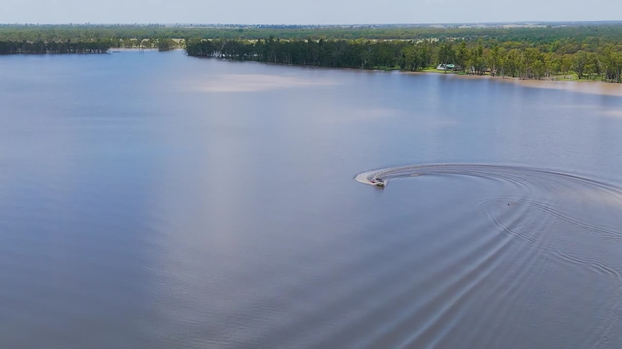 A boat glides across a tranquil lake, leaving ripples in its wake under a clear sky.