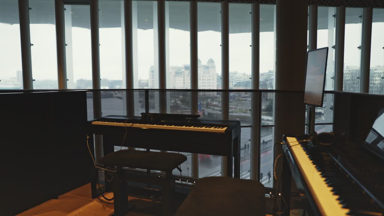 A black upright piano near large windows in the library, offering a quiet artistic space for visitors