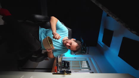 VERTICAL-Young-freelancer-enjoy-his-lunch-break-eating-healthy-vegan-salad-sitting-on-a-chair-in-professional-home-studio-workplace-with-blue-light-in-background