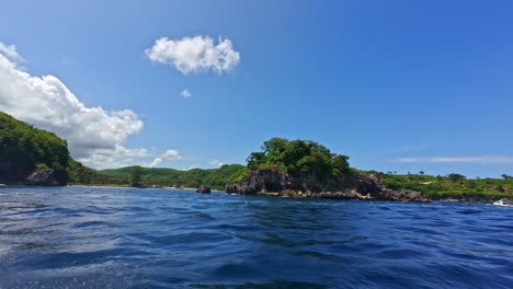lush green island nusa penida in indonesia with rocky shores surrounded by ocean waters. pov from boat. wide shot